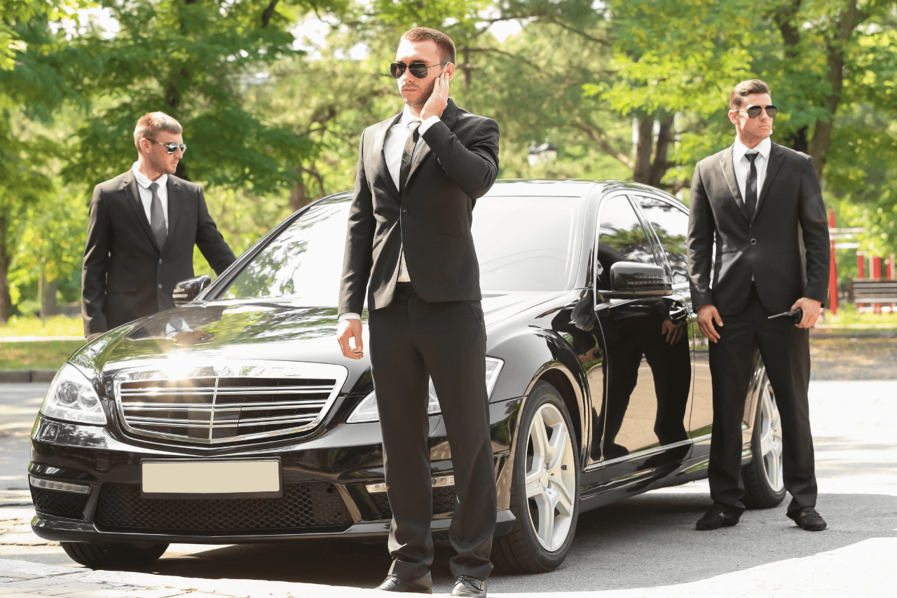 Executive protection officers standing by a black sedan during client transport